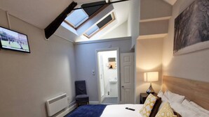Un dormitorio con cama, mesita de noche, lámpara, silla, ventana y puerta que da al baño.