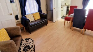 A living room with a sofa, a coffee table, and a dining area with chairs. - Stay Norwich Apartments Cathedral Quarter (Norwich)