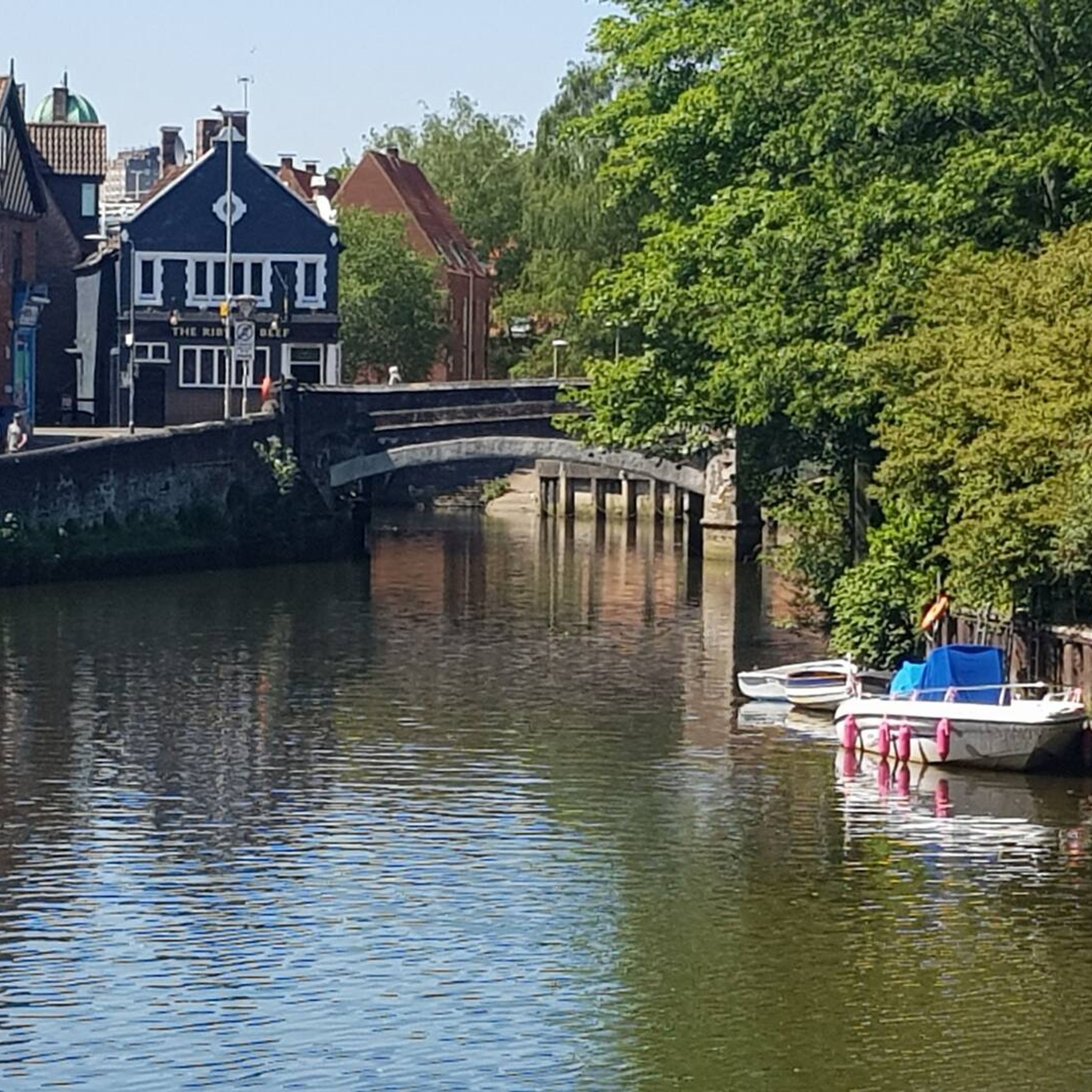 A canal with a stone bridge, boats, and a building with a sign that reads "The Rib."