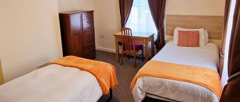A hotel room with two beds, a desk, a chair, a lamp, and artwork on the walls.