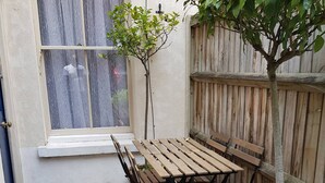 A patio with a wooden table and chairs, a small tree, and a wooden fence. - Stay Norwich Apartments Cathedral Quarter (Norwich)