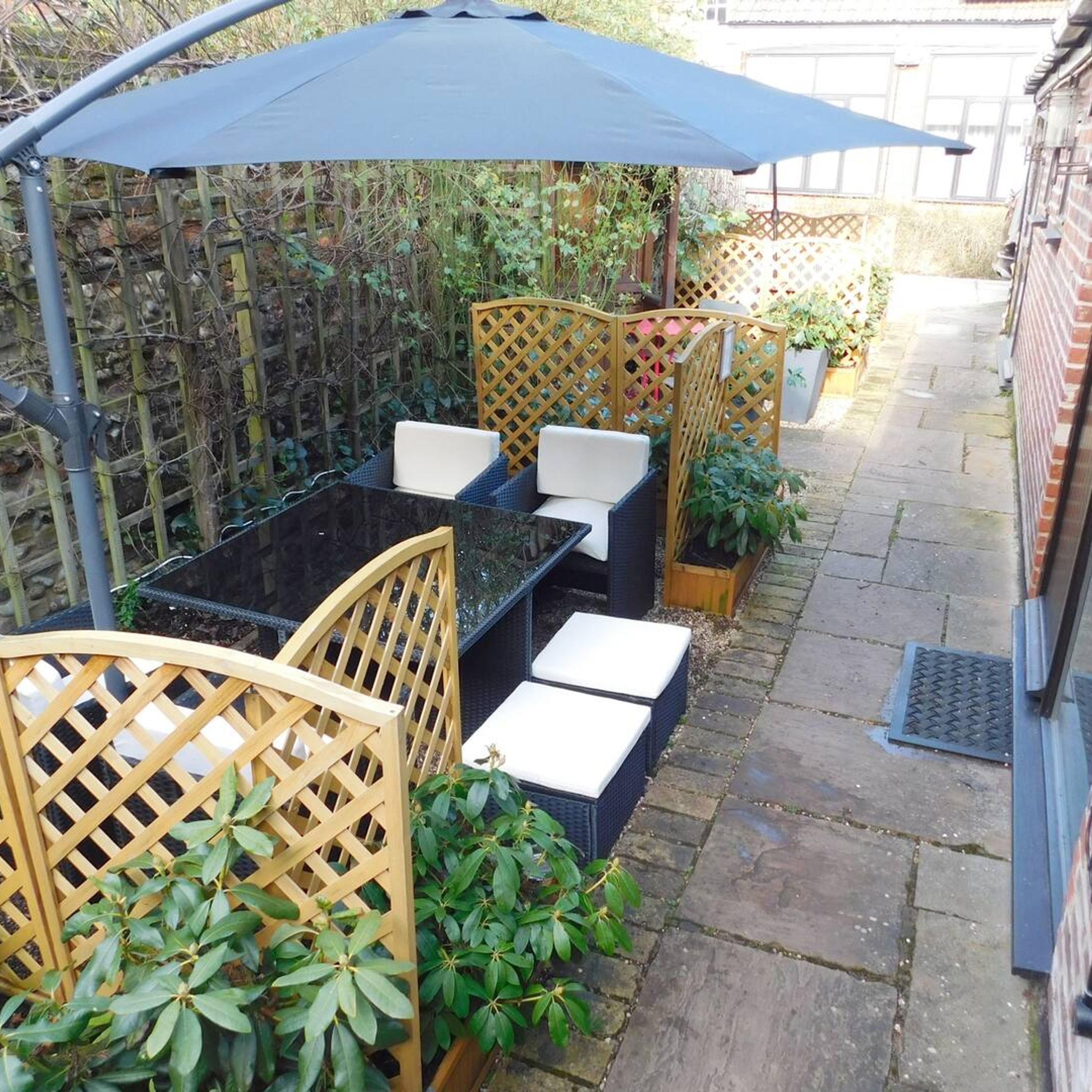 An outdoor seating area with a table and chairs, surrounded by wooden lattice panels and potted plants.