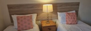 A hotel room with two beds, each with patterned pillows and a nightstand with a lamp.