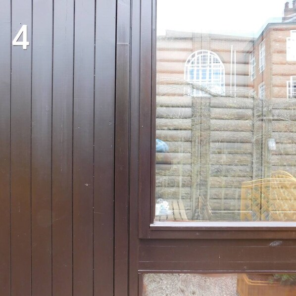 Une porte en bois portant le numéro 4, une fenêtre qui reflète un bâtiment à l’architecture incurvée et une clôture.
