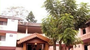 Un edificio de varios pisos con una entrada central, rodeado de follaje y árboles.