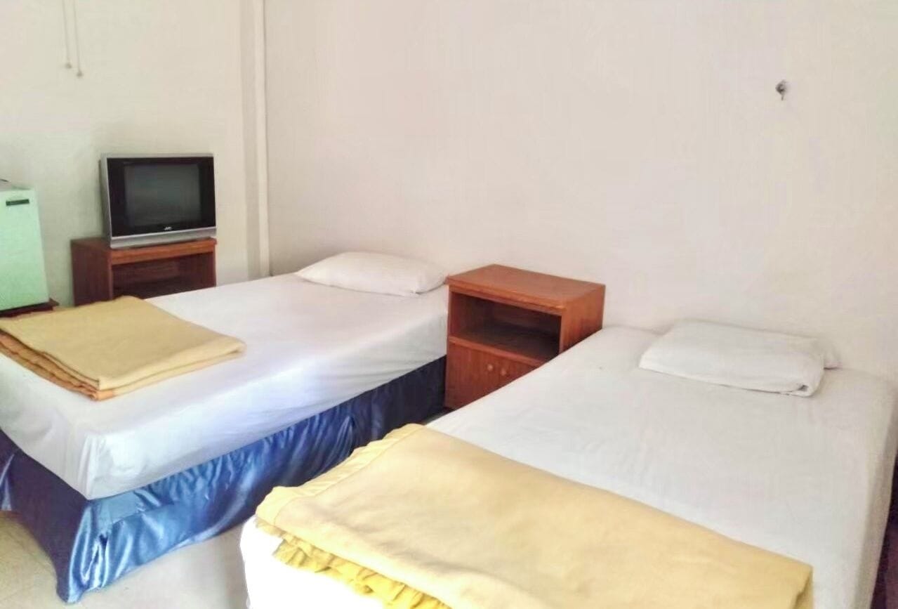 Una habitación con dos camas, un televisor sobre un mueble bajo y un pequeño armario de madera.
