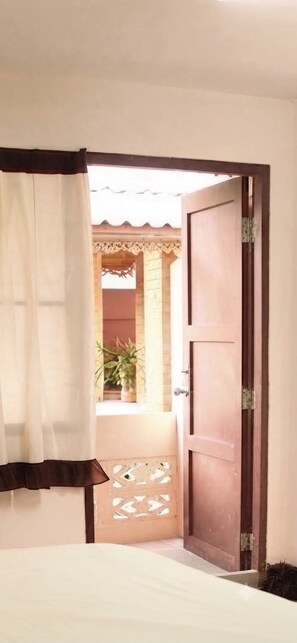Una habitación con una cama, una puerta de madera y vistas a un patio con plantas.
