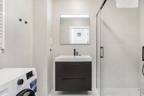 A modern bathroom with a built-in washing machine, a large mirror, and a glass shower enclosure. - ShortStayPoland Zdziechowskiego B153 (Warsaw)