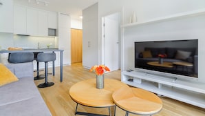 Un salon moderne avec un canapé, une table basse ornée d’un vase de fleurs, un téléviseur et, au fond, un coin cuisine.
