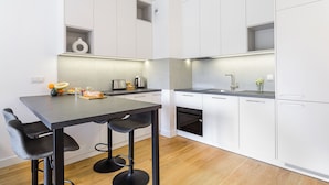 Une cuisine moderne avec des meubles blancs, un plan de travail foncé et un tabouret de bar.