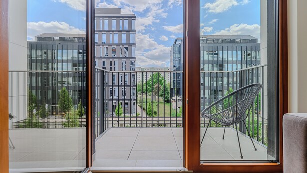 Un balcon donnant sur des immeubles modernes, avec une chaise en métal.