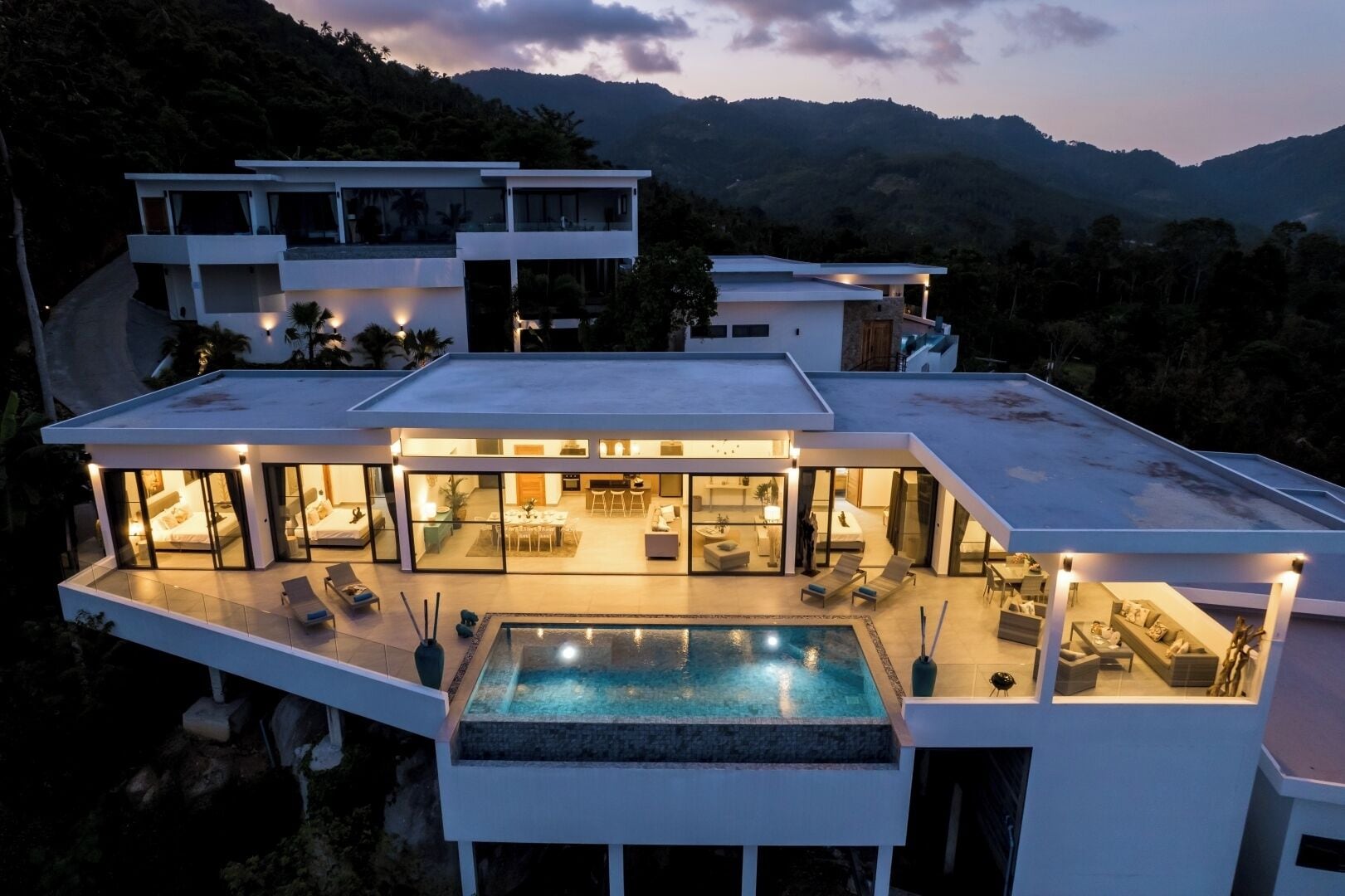 Uma casa moderna de vários andares com piscina no terraço, grandes janelas de vidro e vista para as colinas ao redor.