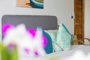 A bed with patterned pillows, a grey headboard, and a painting on the wall.