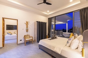 Ein modernes Schlafzimmer mit einem großen Bett, einer Sitzecke und Blick ins Freie.