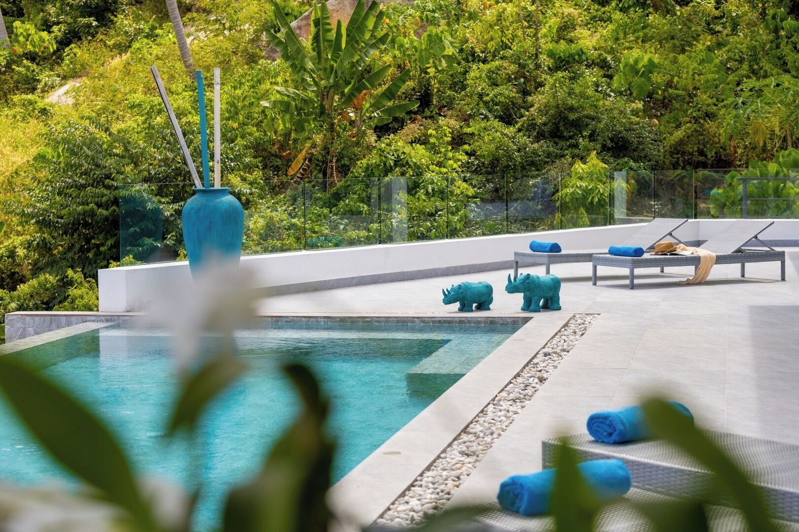 A pool with a clear view of the surrounding greenery, a modern lounge area with sun loungers, and decorative animal figures.