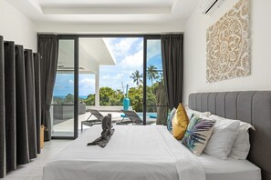 A modern hotel room with a large bed, a view of the ocean, and a balcony with outdoor furniture.