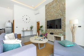 Ein modernes Wohnzimmer mit einer Wand aus Stein, einem Flachbildfernseher und einem runden Couchtisch mit Dekorationselementen.