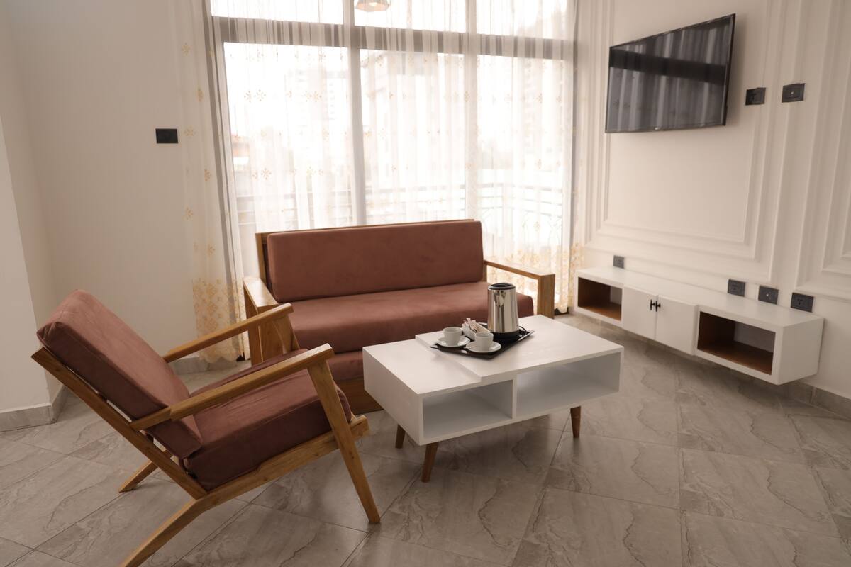 Ein modernes Wohnzimmer mit Sofa, Sessel, Couchtisch und einem an der Wand befestigten Flachbildfernseher.