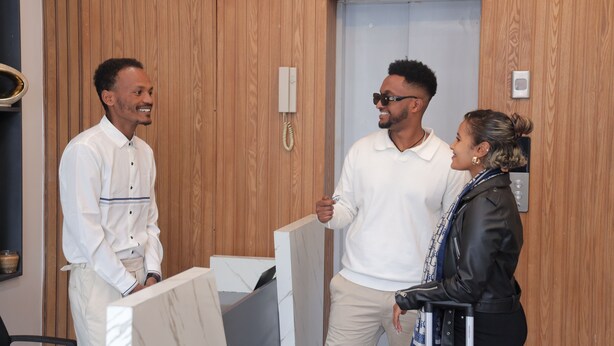 Three people in a wooden-paneled room with a white door, a wall-mounted phone, and a small shelf with a jar. - Yohannes Guesthouse Addis (Addis Ababa)