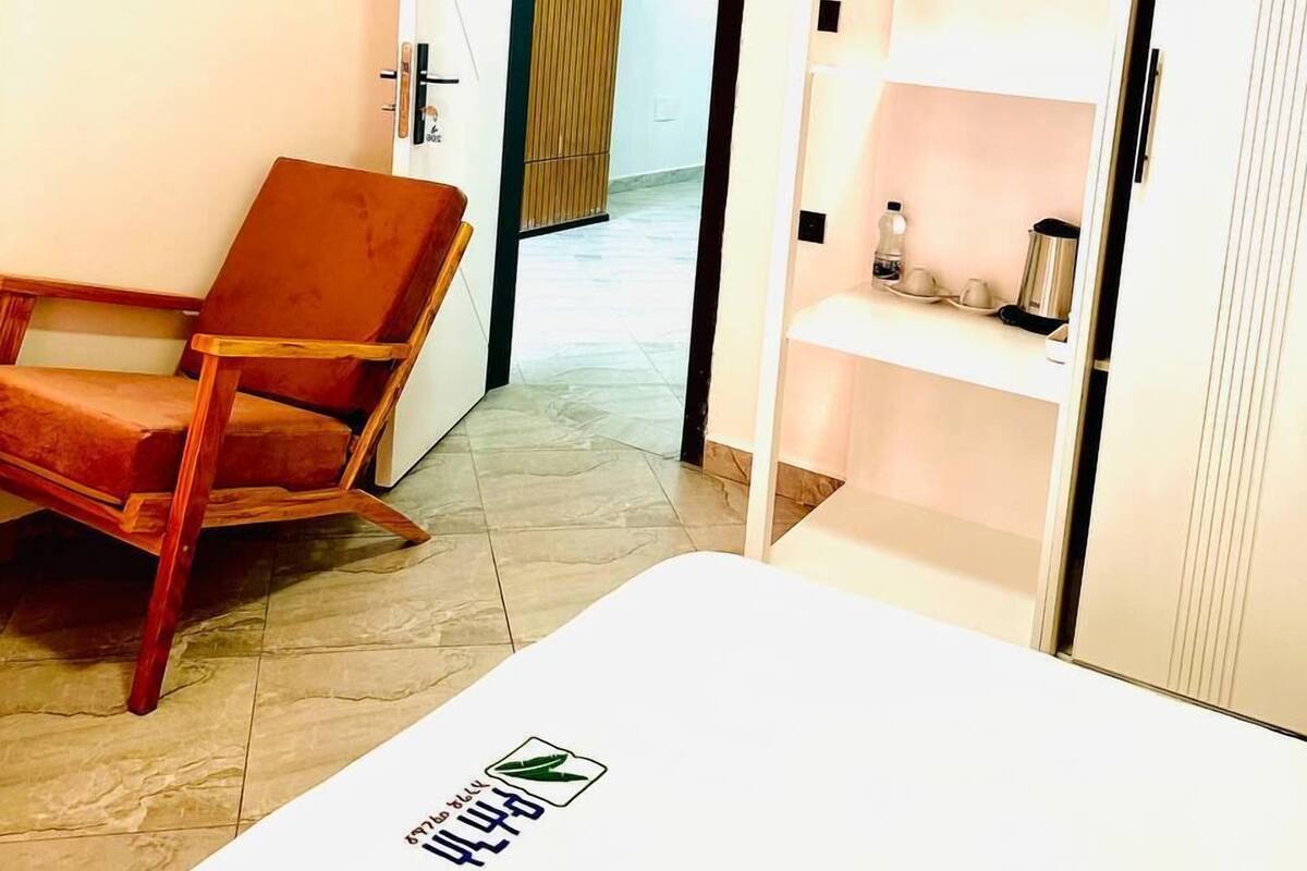 Ein Hotelzimmer mit einem Holzstuhl, einem weißen Bett und einem Schrank mit Regalen.
