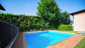 Una piscina rettangolare con bordo piastrellato, circondata da una recinzione e vegetazione.