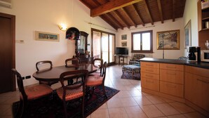 Zona pranzo con tavolo e sedie in legno, un divano e angolo cottura con pensili e una macchina per il caffè.