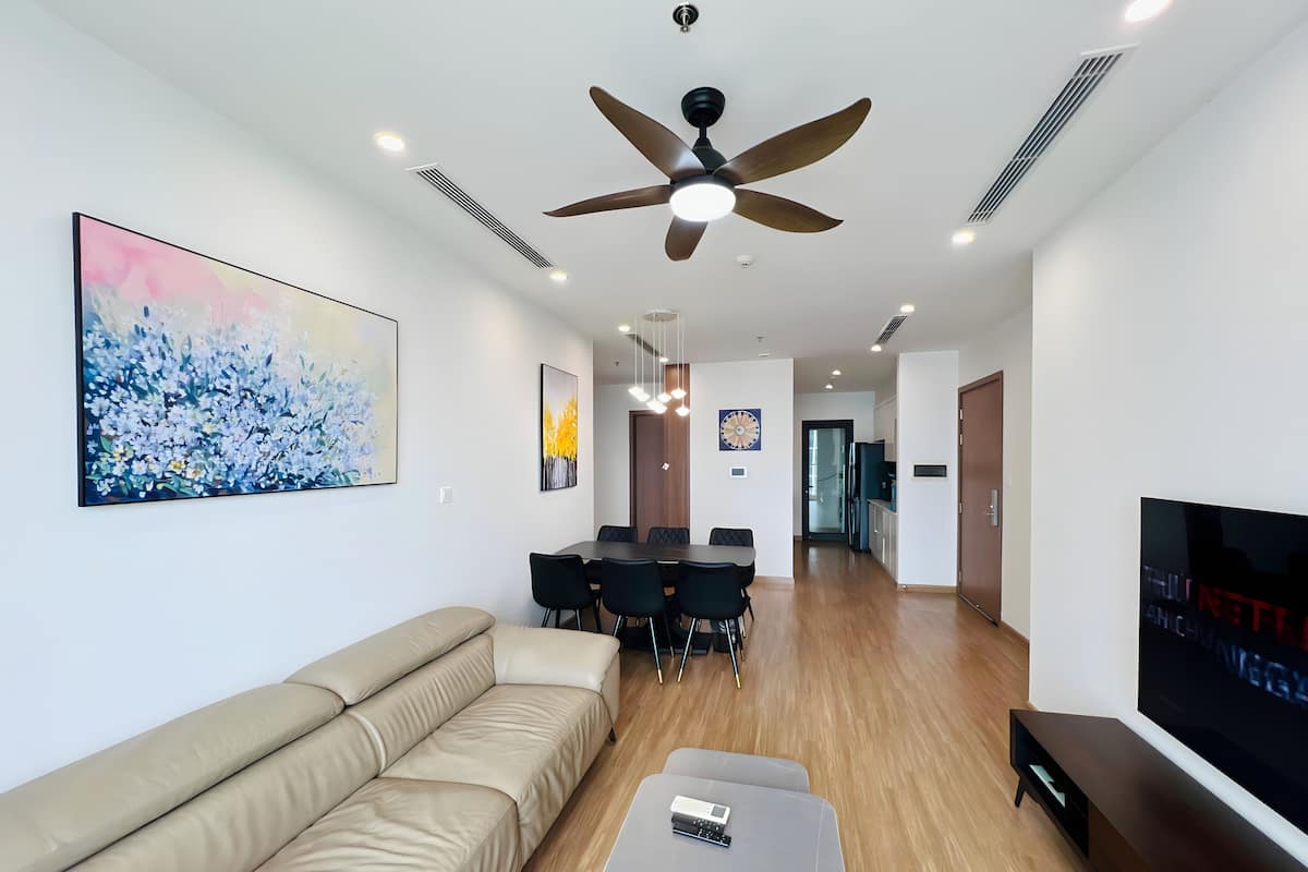 Un salon moderne avec un canapé beige, une table à manger avec des chaises, un ventilateur de plafond et un téléviseur à écran plat.