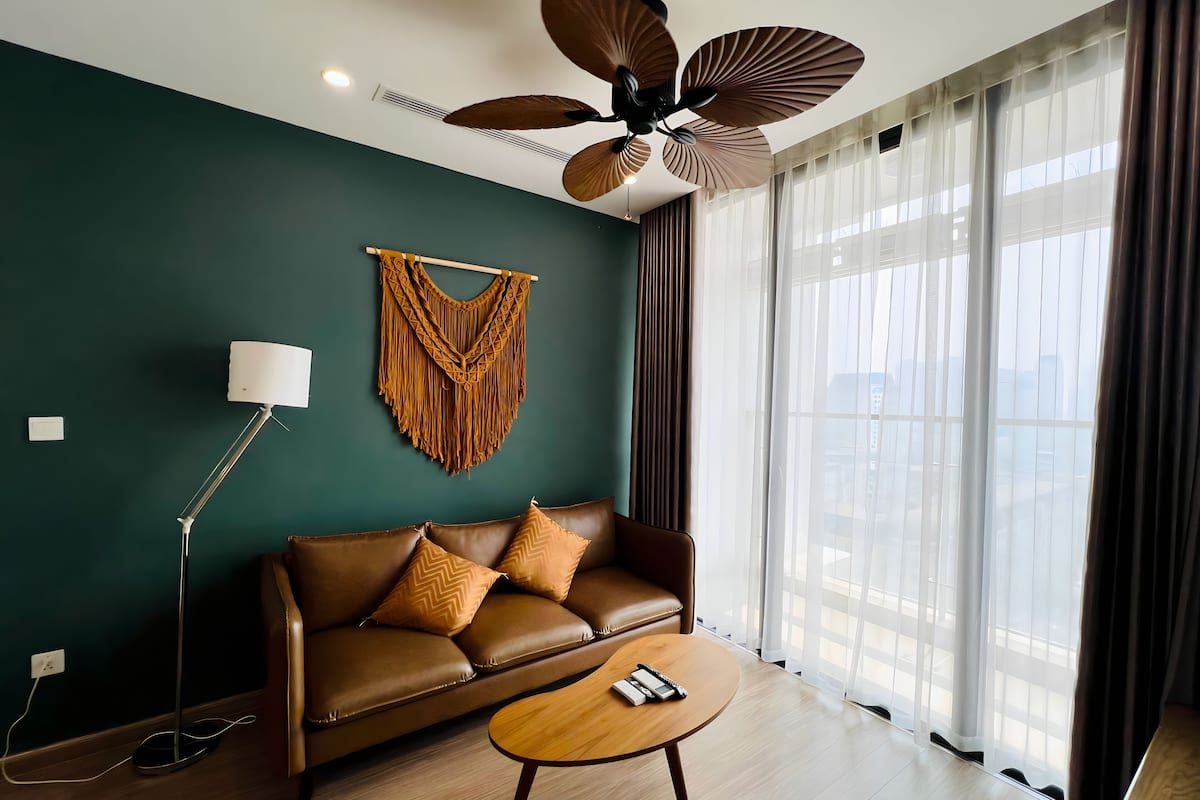 Un salon moderne avec un canapé en cuir marron, une table basse en bois, un lampadaire et un ventilateur de plafond.