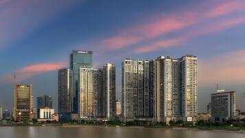 Un horizonte urbano con edificios modernos y altos, un río en primer plano y un cielo despejado con nubes rosadas.