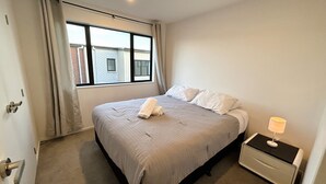 Een hotelkamer met een groot bed, een nachtkastje met een lamp en een raam met gordijnen.