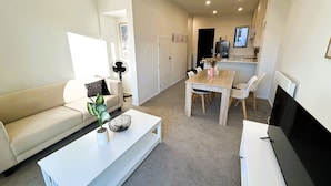 Een moderne woonkamer met een bank, een salontafel met decoratieve voorwerpen, een eethoek met een tafel en stoelen, en een keuken met een koelkast en een televisie.