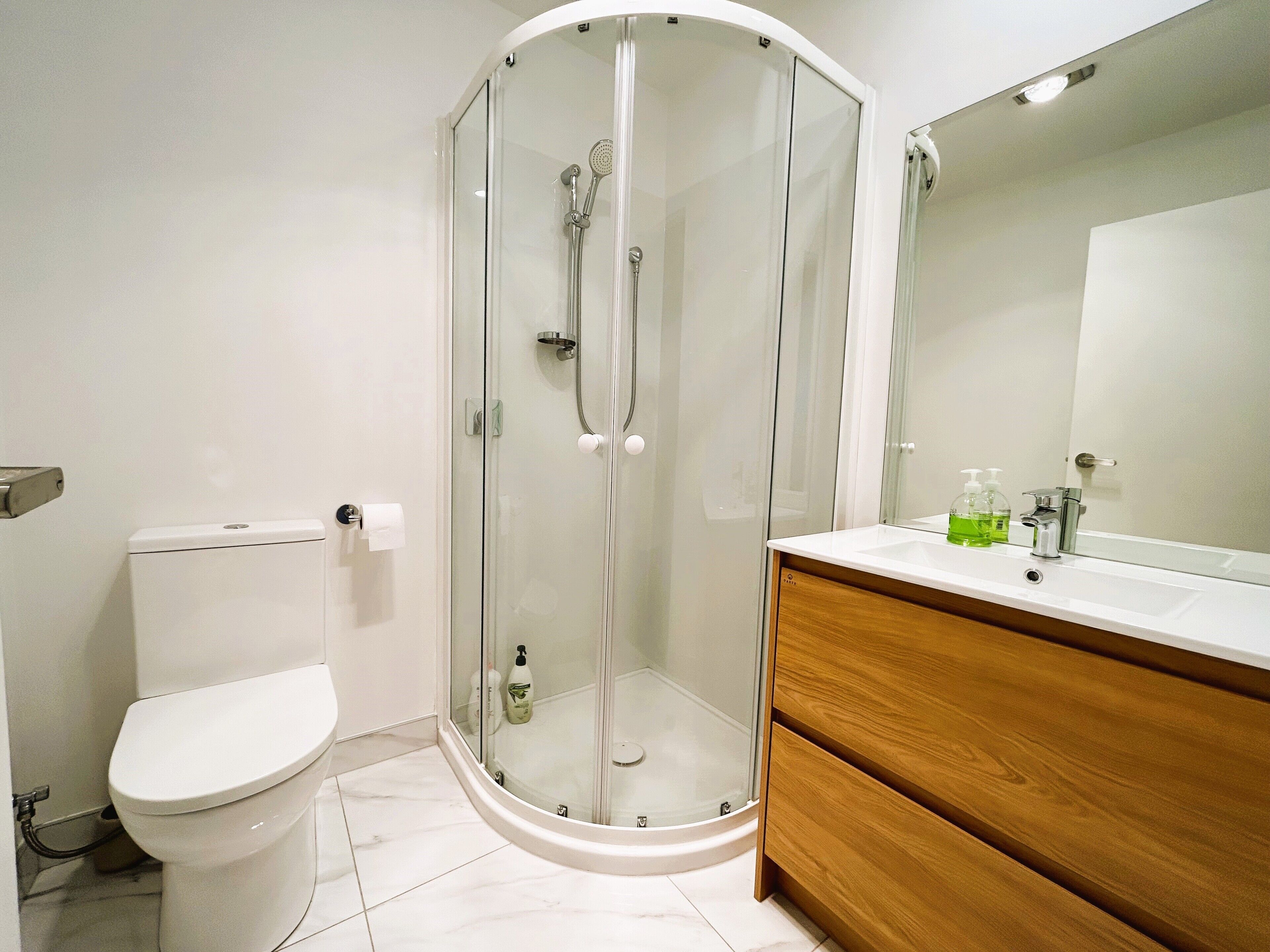 A modern bathroom with a glass-enclosed shower, a toilet, and a vanity with a mirror.