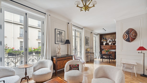 A spacious living room with a billiards table, plush armchairs, and a view of the city through large windows.