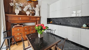 A modern kitchen with white cabinets, a marble countertop, and a wooden dining table with chairs.