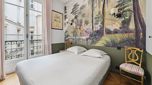 A bedroom with a bed, a chair, a mural, and a window with curtains.