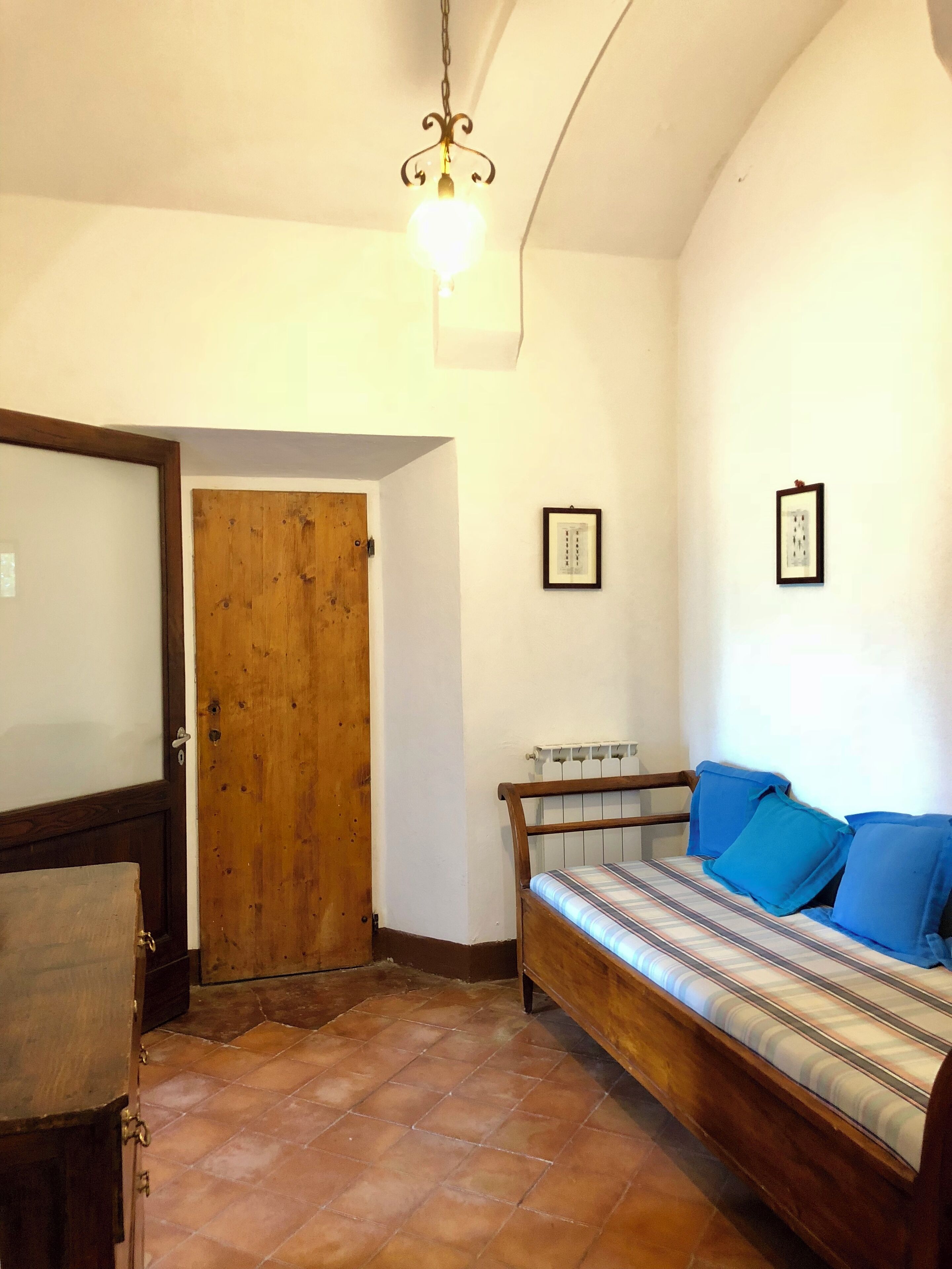 Un dormitorio con puerta de madera, cama con almohadas azules, radiador y lámpara colgante.