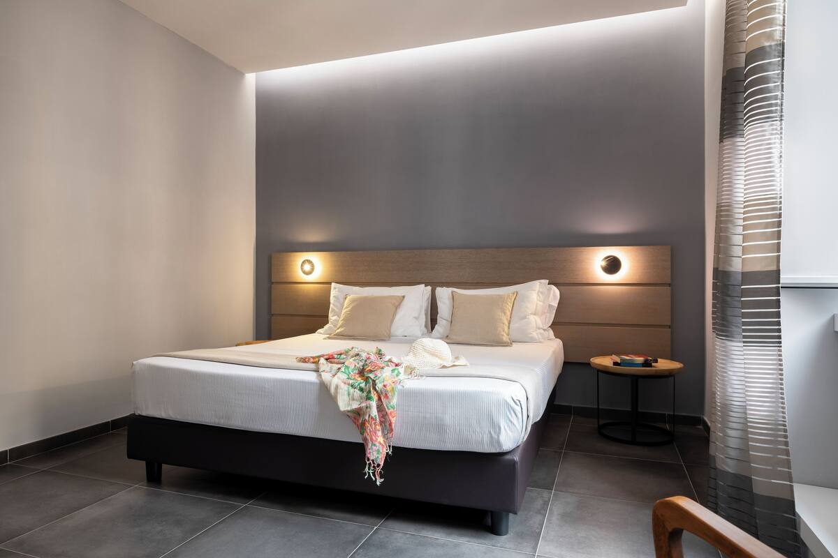 A modern bedroom with a large bed, a bedside table, and a headboard with integrated lighting.