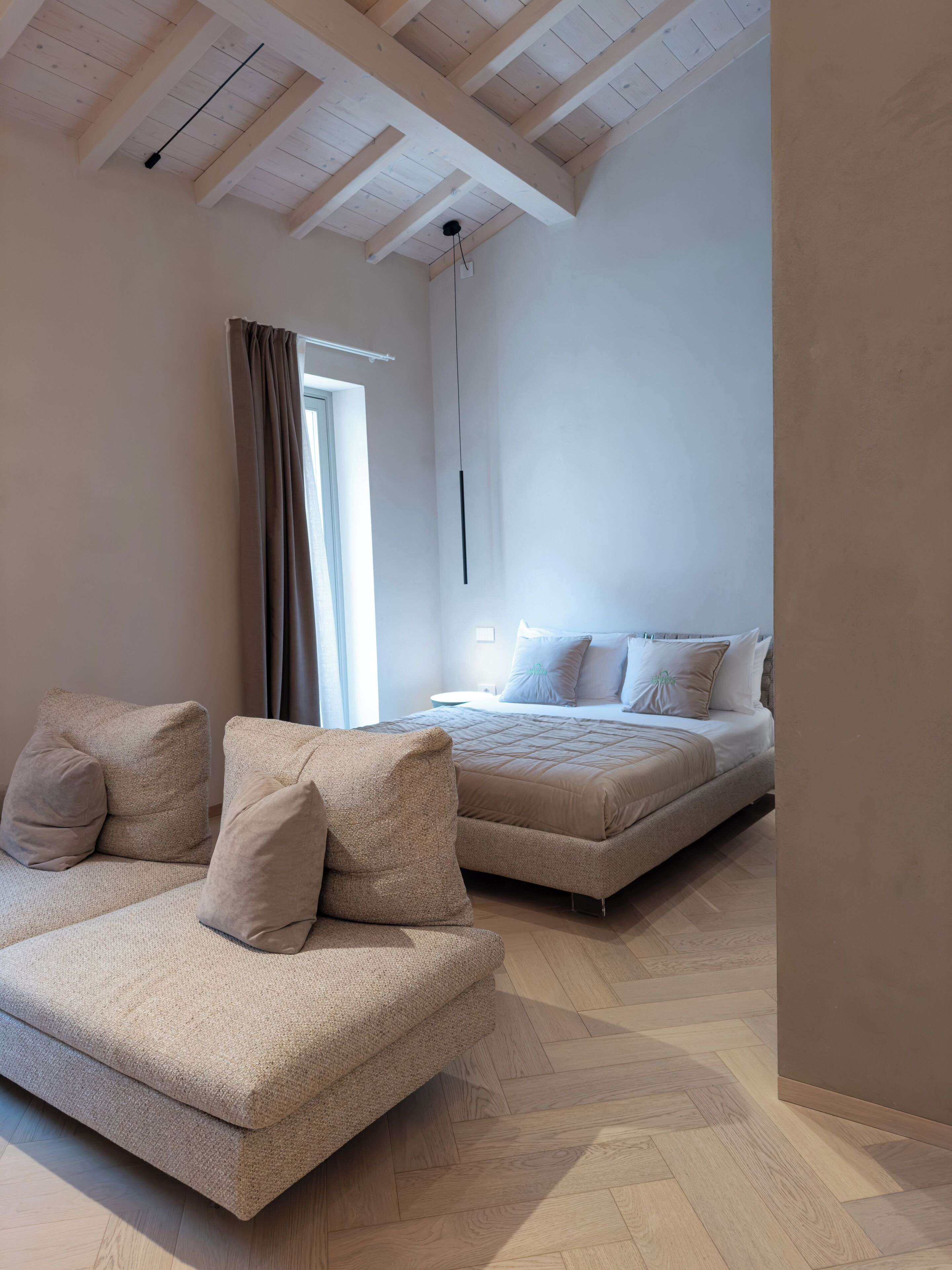A bedroom with a large bed, a sofa, and a hanging light fixture.