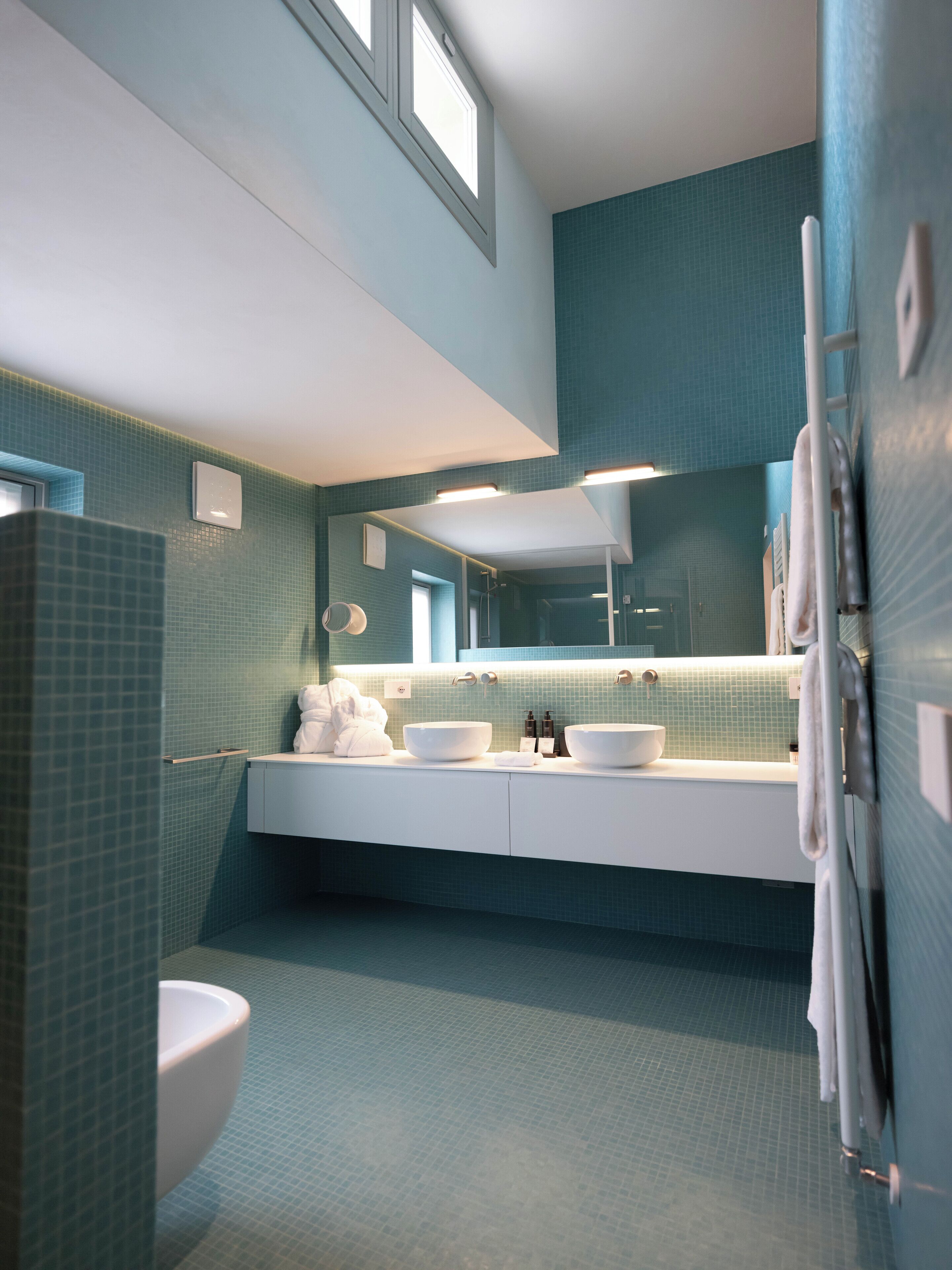 A modern bathroom with a large mirror, two sinks, and a toilet.