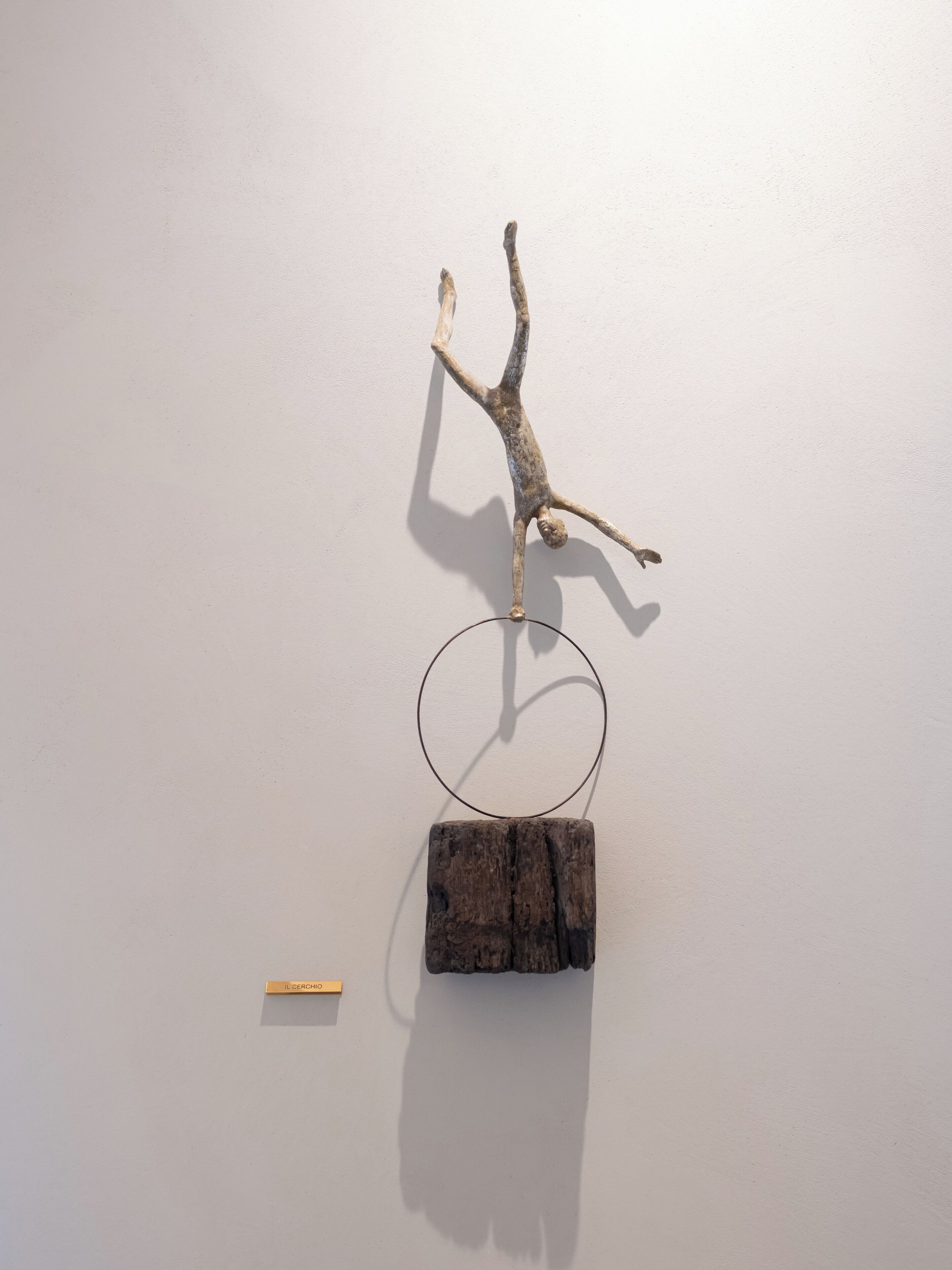 Una scultura raffigurante una figura umana in una posa dinamica, montata su un muro con una cornice metallica circolare sottostante.