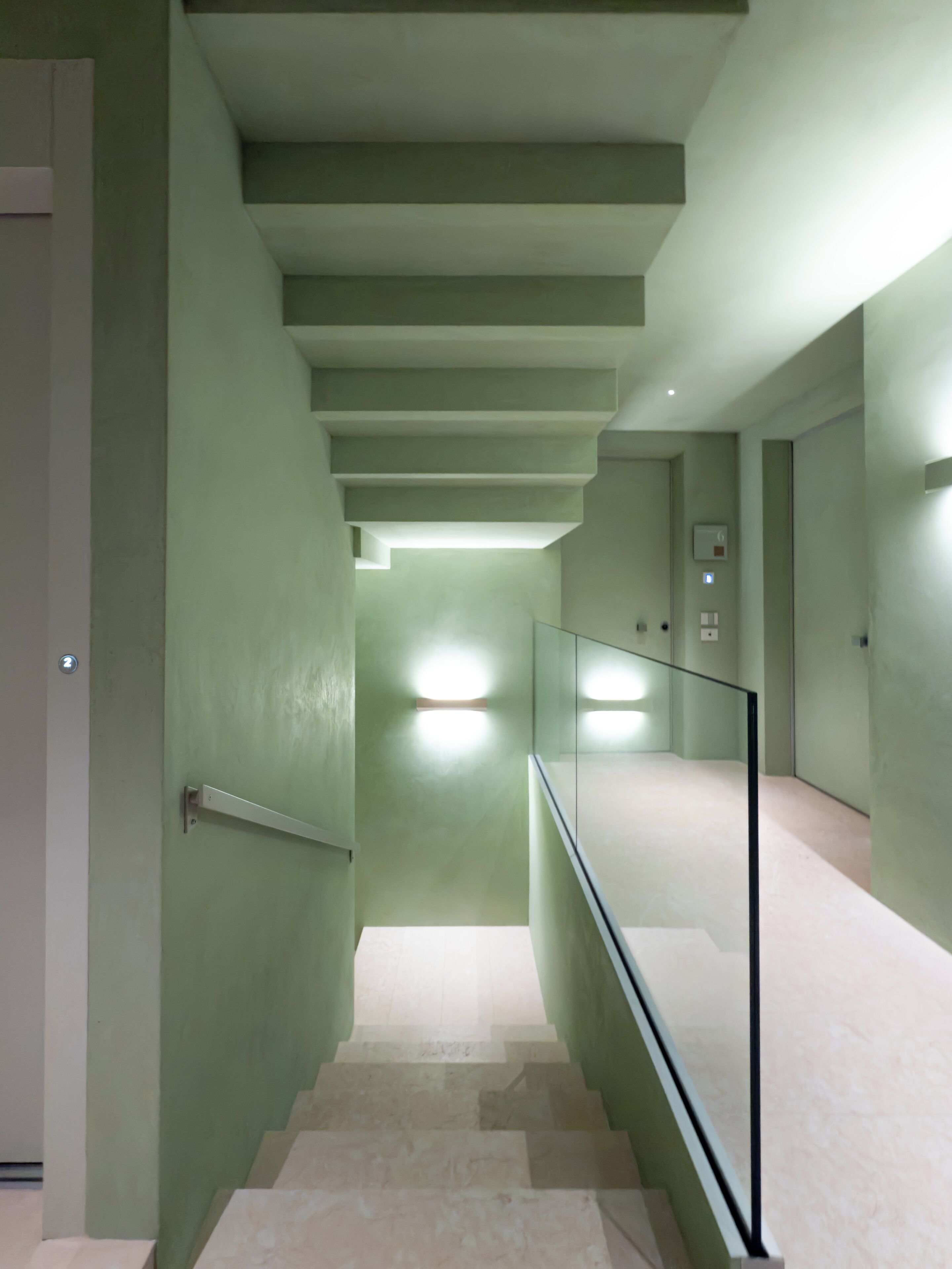 Un intérieur moderne avec un escalier, une rampe en verre et des murs verts.