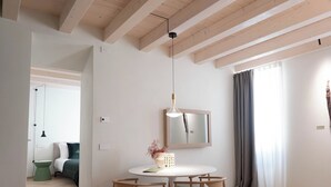 A modern, well-lit room with a wooden ceiling, a round dining table with chairs, a small side table, and a mirror on the wall. - Palazzo Ciopeta (Verona)