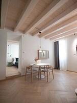 A modern, well-lit room with a wooden ceiling, a round dining table with chairs, a small side table, and a mirror on the wall.