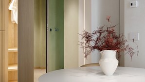 A modern dining area with a round white table, a white vase with red foliage, and a hanging pendant light. - Palazzo Ciopeta (Verona)
