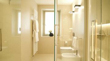 A modern bathroom with a glass shower enclosure, a toilet, a bidet, and a sink.