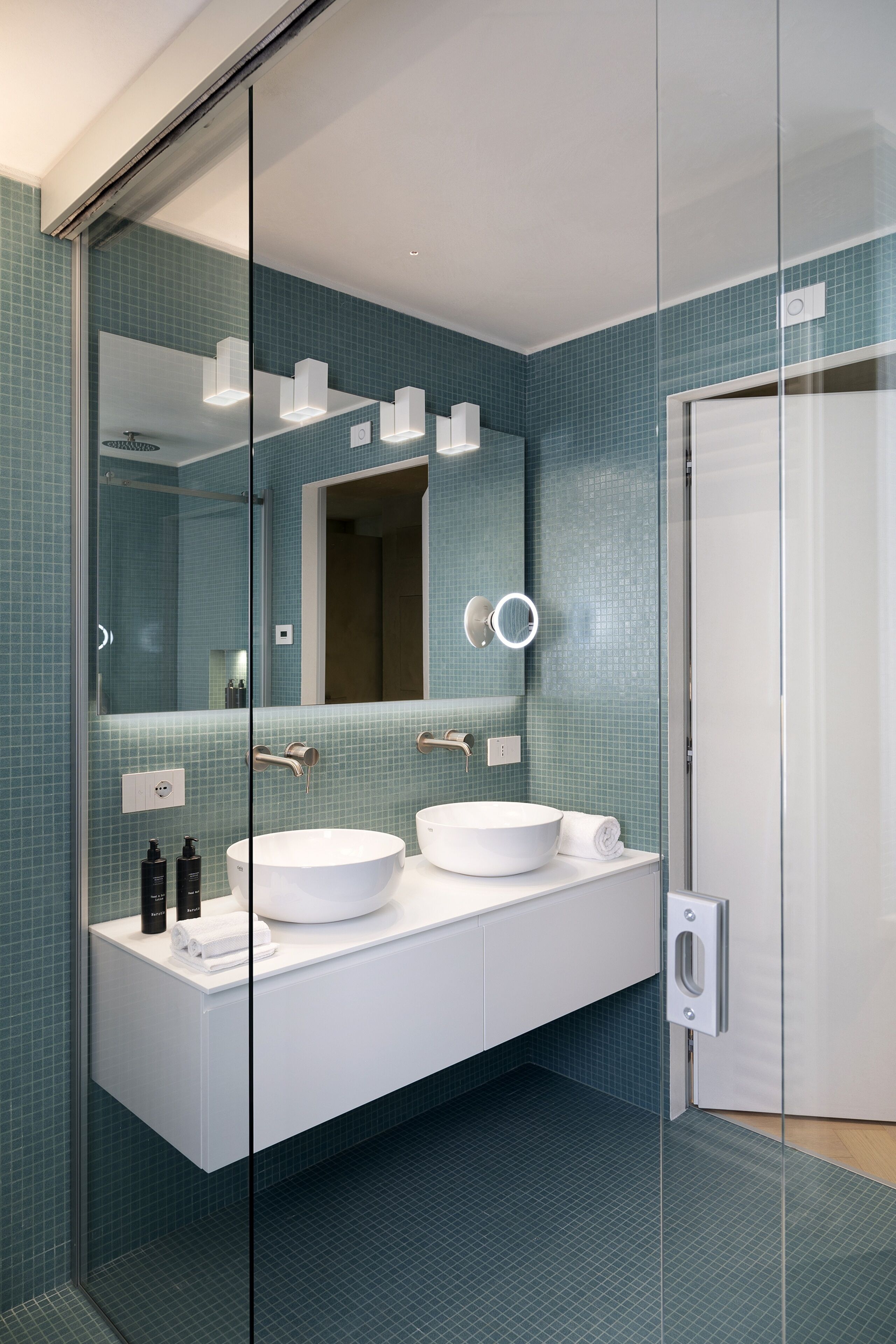 Ein modernes Badezimmer mit Duschkabine aus Glas, zwei weißen Waschbecken und einem großen Spiegel.