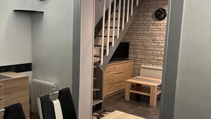 Un área de comedor moderna con una mesa y sillas de madera, una escalera que conduce a un altillo y una pared de ladrillo.