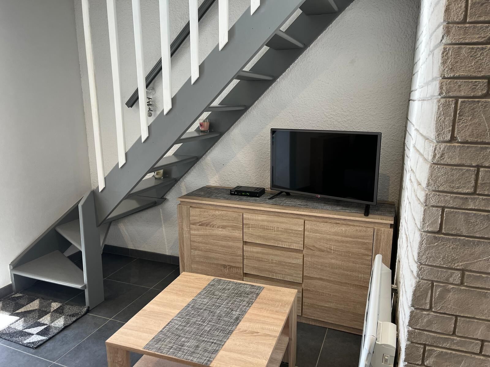 A modern staircase with a TV on a wooden cabinet, a small table, and a patterned rug.