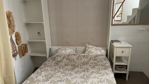 Una cama bien hecha con una colcha de estampado floral, una mesita de noche con un libro y un espejo en la pared.