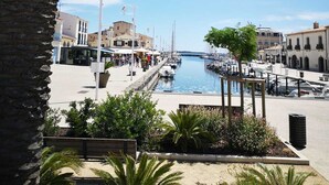 Un puerto deportivo con barcos amarrados, un paseo marítimo y edificios al fondo.